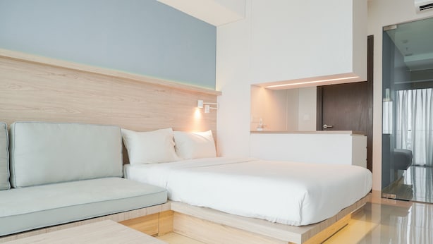 Una habitación de hotel moderna con una cama, un sofá, una mesita de noche y un espejo.