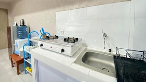Een keuken met witte tegels, een gasfornuis, een spoelbak en een waterdispenser.