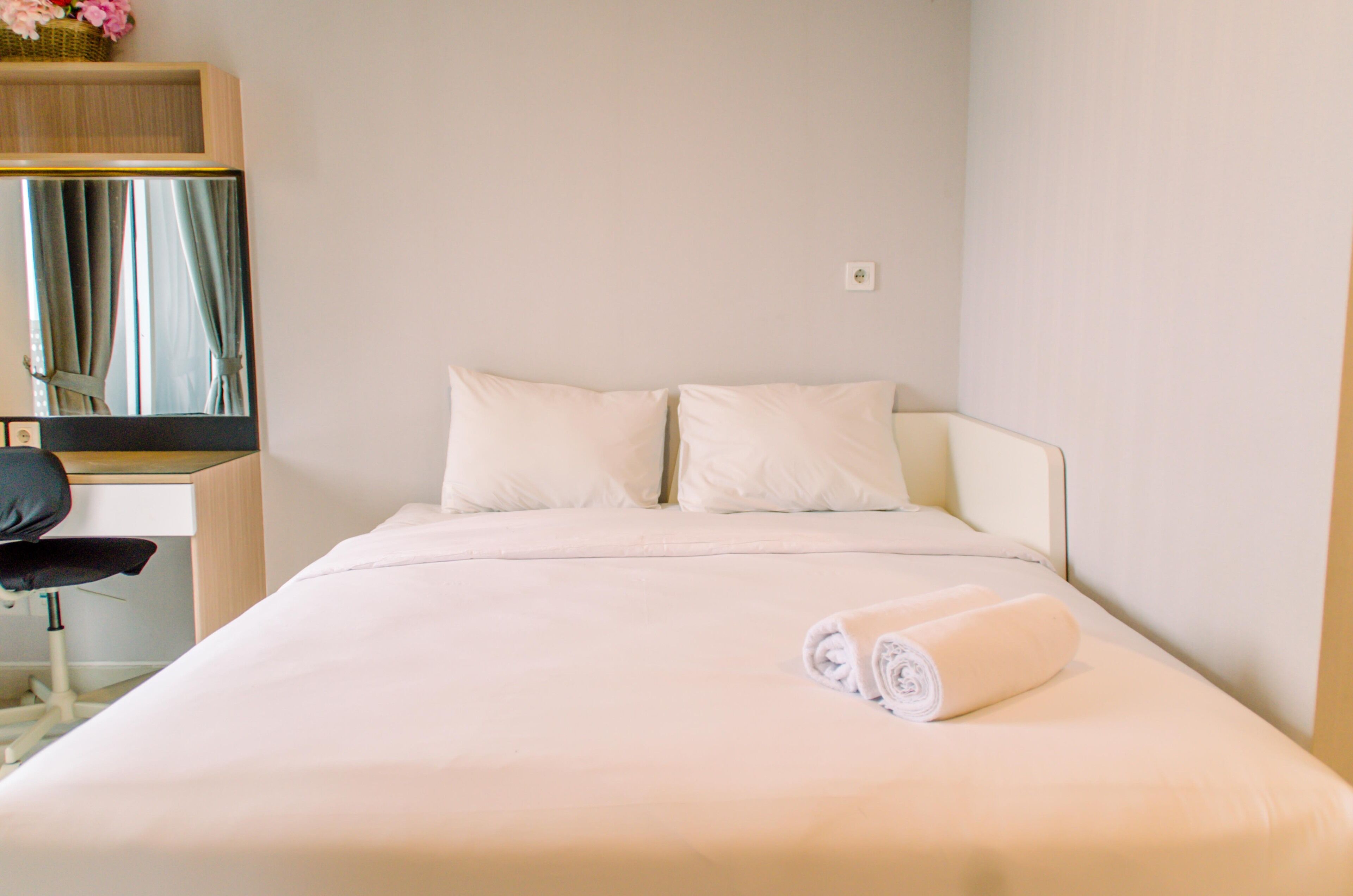 Ein ordentlich bezogenes Bett mit weißen Leinentüchern und zwei Kissen, ein kleiner Nachttisch mit Lampe und ein Spiegel darüber.