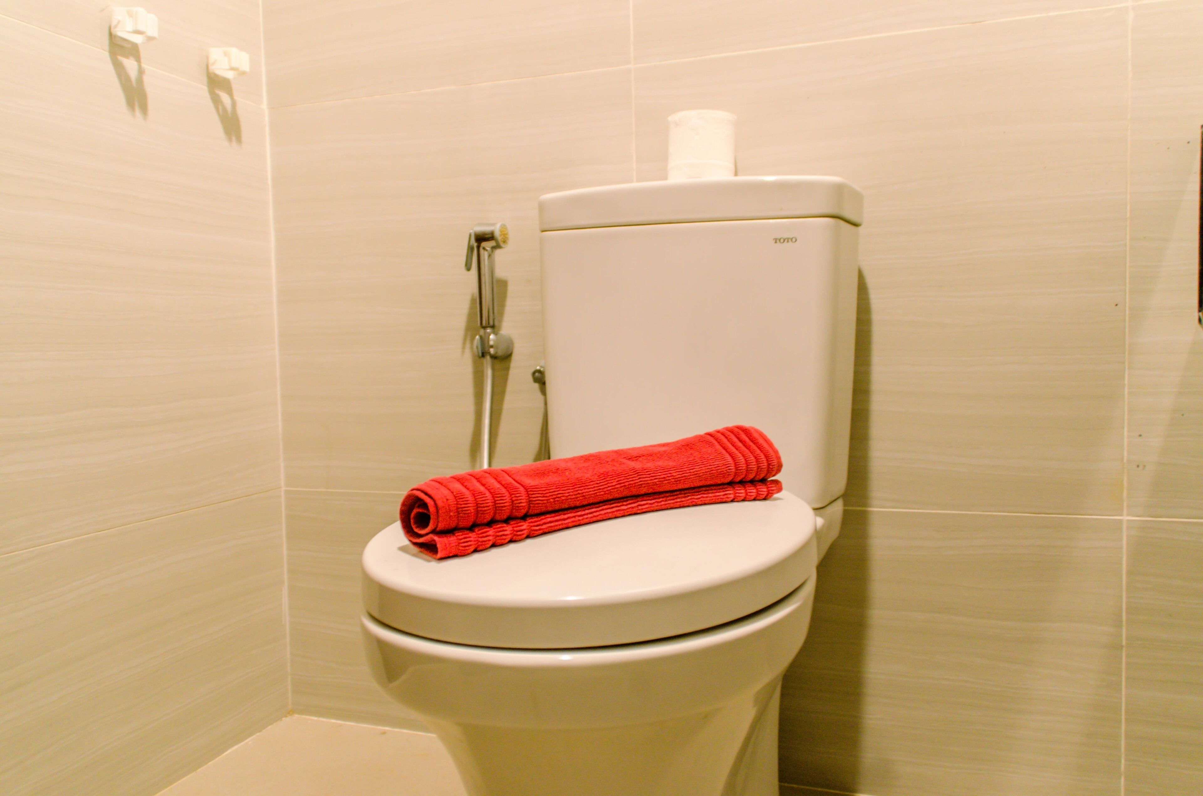 Un inodoro con una toalla roja sobre la tapa y un dispensador de papel higiénico en la pared.