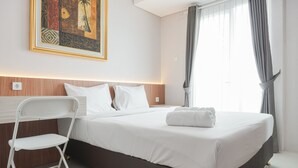 A neatly made bed with white linens, a white chair, and a painting on the wall. - Comfortable and Minimalist Studio Apartment at Woodland Park Residence (Jakarta)