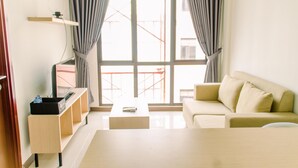 A modern living room with a sofa, a coffee table, and a TV on a stand. - Simply Cozy 1BR at Asatti Apartment (Pagedangan)