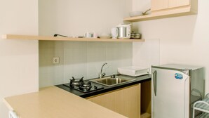 A compact kitchen with a sink, stove, and a small refrigerator. - Simply Cozy 1BR at Asatti Apartment (Pagedangan)