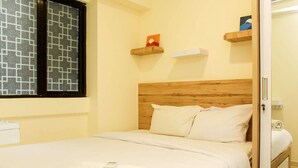 A neatly made bed with white linens, a wooden headboard, and a window with a geometric pattern. - Cozy Living and Tidy 1BR Meikarta Apartment (Cikarang)