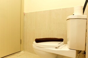 Sanitário com toalha castanha no assento, paredes bege e porta fechada.