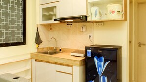 A compact kitchen with a sink, microwave, and a refrigerator with a floral design. - Cozy Living and Tidy 1BR Meikarta Apartment (Cikarang)