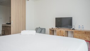 Une chambre d’hôtel avec un lit, un bureau en bois sur lequel se trouve une télévision, et une salle de bain visible à travers une porte ouverte.