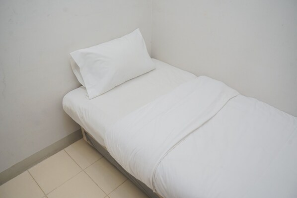 Una habitación pequeña con cama individual, ropa de cama blanca y una pared lisa.