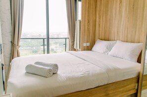 A neatly made bed with white linens and two rolled towels, a wooden headboard, and a view of a cityscape through large windows.
