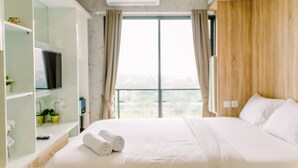 A hotel room with a bed, a TV, a shelf with plants, and a window with curtains. - Cozy and Simply Studio at Sky House BSD Apartment (Pagedangan)