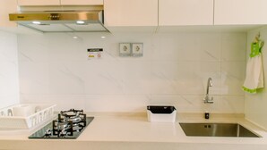 A modern kitchen with a gas stove, stainless steel sink, and white cabinets. - Cozy and Simply Studio at Sky House BSD Apartment (Pagedangan)