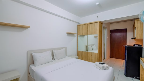 A hotel room with a bed, a wooden wardrobe, a mirror, a small table, and a fan. - Modern and Homey Studio at Gunung Putri Apartment (Gunung Putri)