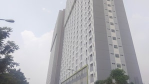 A tall, modern building with a grid-like facade and evenly spaced windows. - Modern and Homey Studio at Gunung Putri Apartment (Gunung Putri)