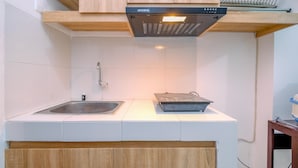 A compact kitchen with white tiles, a stainless steel sink, a wooden countertop, and a black range hood. - Modern and Homey Studio at Gunung Putri Apartment (Gunung Putri)