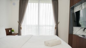 A hotel room with a large bed, a TV mounted on the wall, and a window with curtains.
