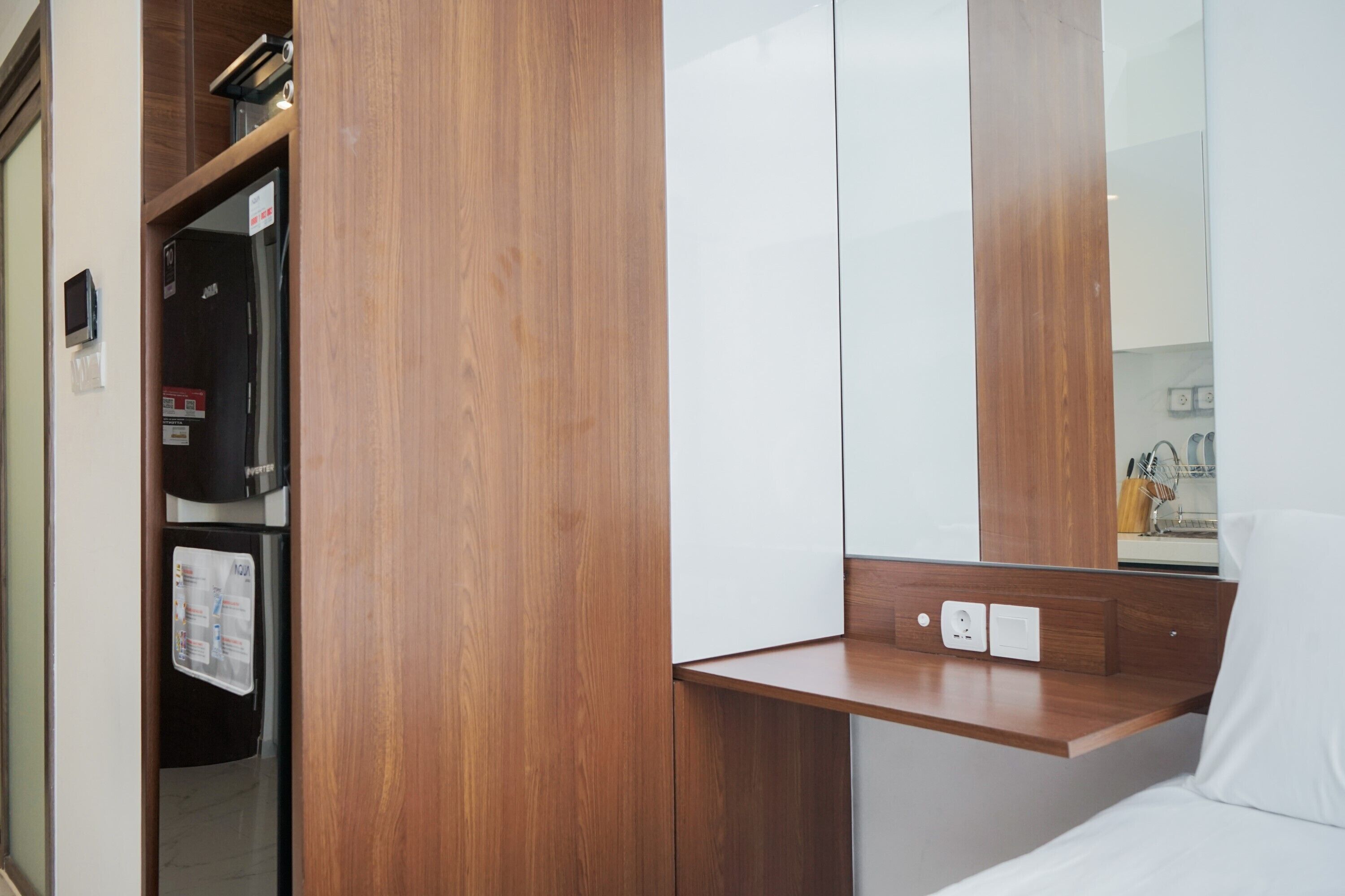 Een hotelkamer met een houten garderobe, een klein houten plankje en een wit bed.