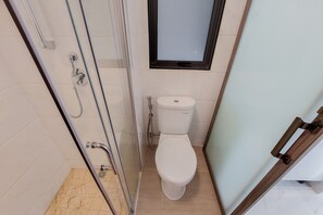 A bathroom with a glass-enclosed shower, a toilet, and a window above the toilet. - Comfort 2BR at Sky House BSD Apartment (Pagedangan)