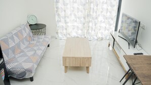 Uma sala de estar minimalista com um sofá, uma pequena mesa redonda com um relógio, uma mesa de centro de madeira, uma TV e uma mesa de jantar.