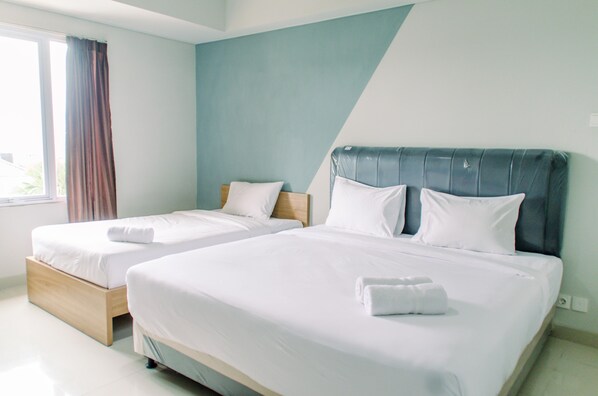 A hotel room with two single beds, a large window with curtains, and a blue accent wall.