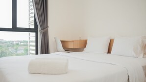 A neatly made bed with a white towel, a wooden nightstand, and a chair. - Fully Furnished with Cozy Design 2BR at Sky House BSD Apartment (Pagedangan)
