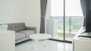 A modern living room with a grey sofa, a white round table, and a TV on a desk. - Fully Furnished with Cozy Design 2BR at Sky House BSD Apartment (Pagedangan)