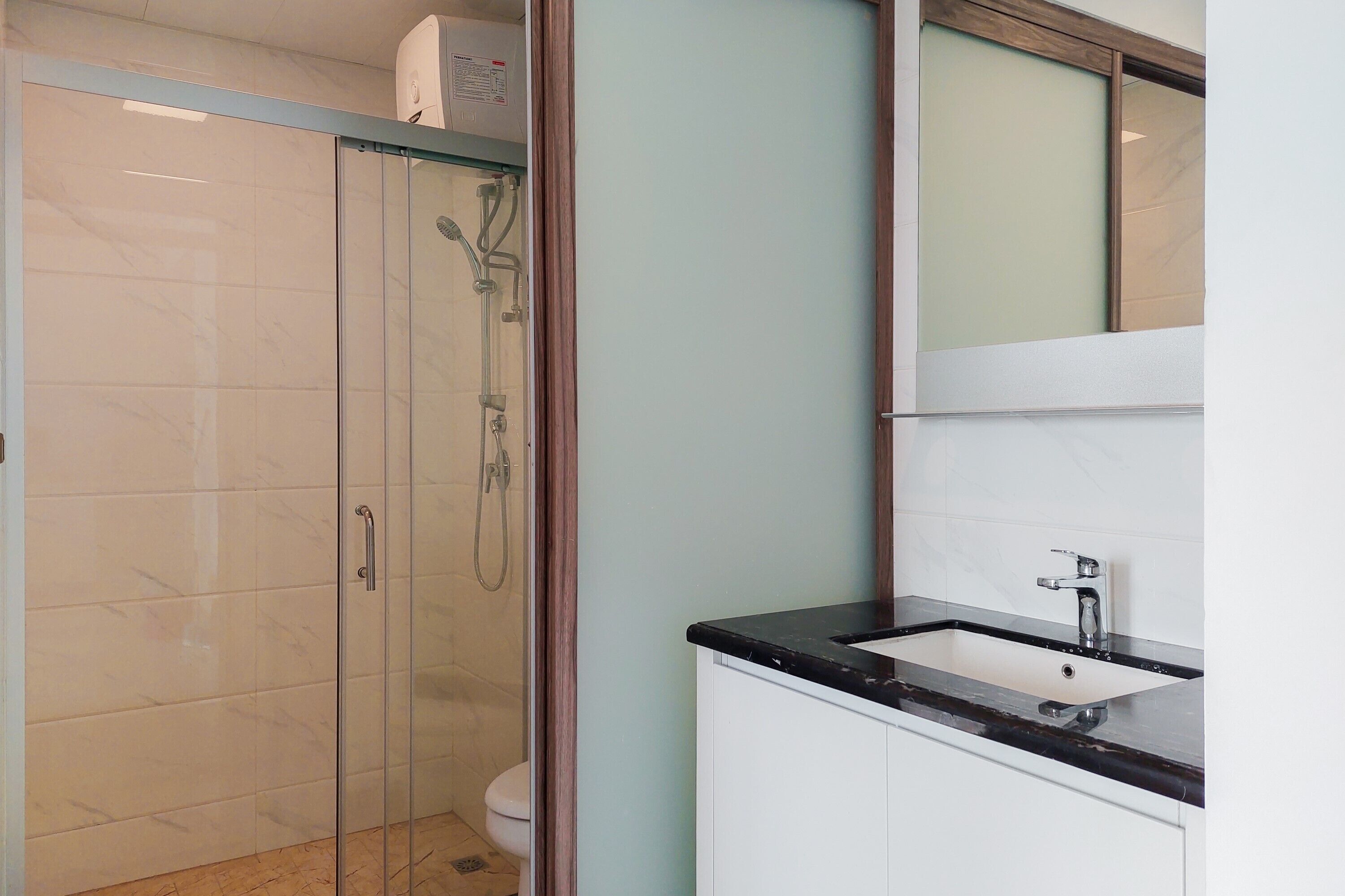 A bathroom with a glass-enclosed shower, a sink with a black countertop, and white cabinets.