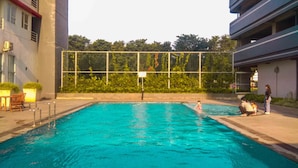A swimming pool with a metal fence, a few people, and a building with balconies.