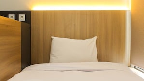 A hotel room with a wooden headboard, a single white pillow, and a neatly made bed.
