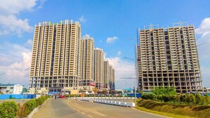A road with two high-rise buildings on either side, one under construction and one completed. - Golden Osaka 2BR Apartment at Meikarta Apartment (Cikarang)