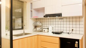 A modern kitchen with white cabinets, a black range hood, a dish rack, a rice cooker, and a coffee maker. - Golden Osaka 2BR Apartment at Meikarta Apartment (Cikarang)