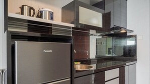 A modern kitchen with a stainless steel refrigerator, dark cabinetry, and a glass backsplash. - Fancy and Nice Studio at West Vista Apartment (Jakarta)