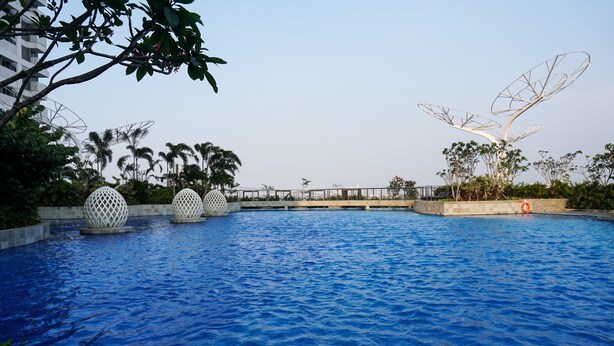 A swimming pool with three spherical water features, surrounded by greenery and a bridge. - Fancy and Nice Studio at West Vista Apartment (Jakarta)