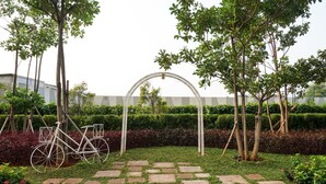 A garden with a paved walkway, a bicycle, and a white arch structure. - Fancy and Nice Studio at West Vista Apartment (Jakarta)
