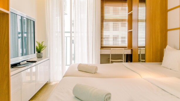 A hotel room with a bed, a desk, a television, and a plant. - Homey and Cozy Stay Studio Room at Serpong Garden Apartmen (Cisauk)