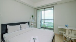 Ein Hotelzimmer mit einem großen Bett, einem Schreibtisch mit zwei Flaschen, einem Sessel und Blick auf Grün durch eine Schiebetür.