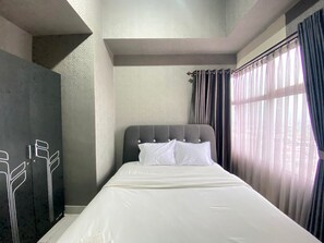 Un dormitorio con cama, armario y ventana con cortinas.
