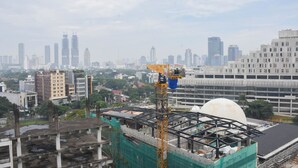 A construction site with a crane and a partially built structure amidst a cityscape with various buildings. - Fully Furnished with Cozy Design Studio at Menteng Park Apartment (Jakarta)