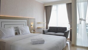 A hotel room with a large bed, a sofa, and a balcony with curtains. - Fully Furnished with Cozy Design Studio at Menteng Park Apartment (Jakarta)