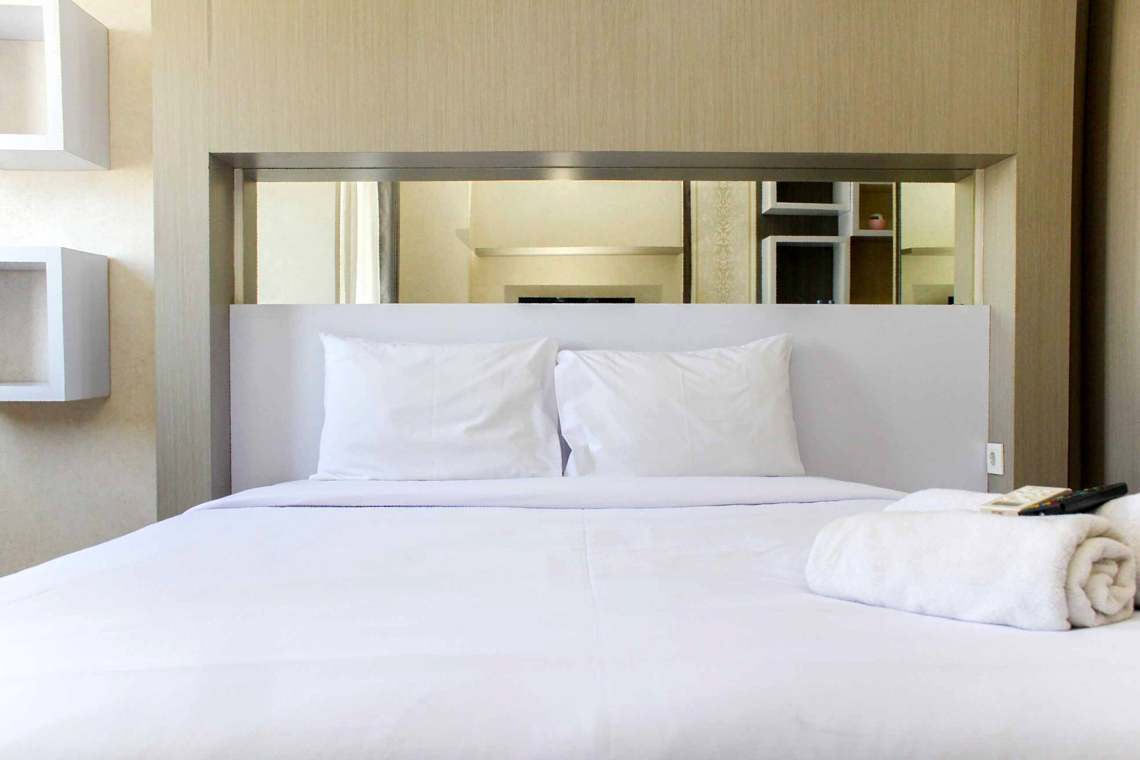 A hotel room with a large bed, white bedding, a remote control, and a rolled towel on the bed.