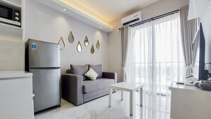 A modern living room with a grey sofa, a white coffee table, and a kitchen area with a refrigerator. - Nice and Elegant 2BR at Sky House BSD Apartment (Pagedangan)