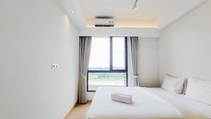 A hotel room with a large bed, a window with curtains, and an air conditioning unit. - Nice and Elegant 2BR at Sky House BSD Apartment (Pagedangan)