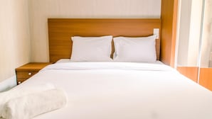 Un lit bien fait, avec du linge de lit blanc et des oreillers, une tête de lit en bois et une table de chevet en bois dotée d’un tiroir.