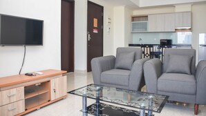Ein modernes Wohnzimmer mit Fernseher, grauen Sofas, einem Glastisch und einer Holzkommode.