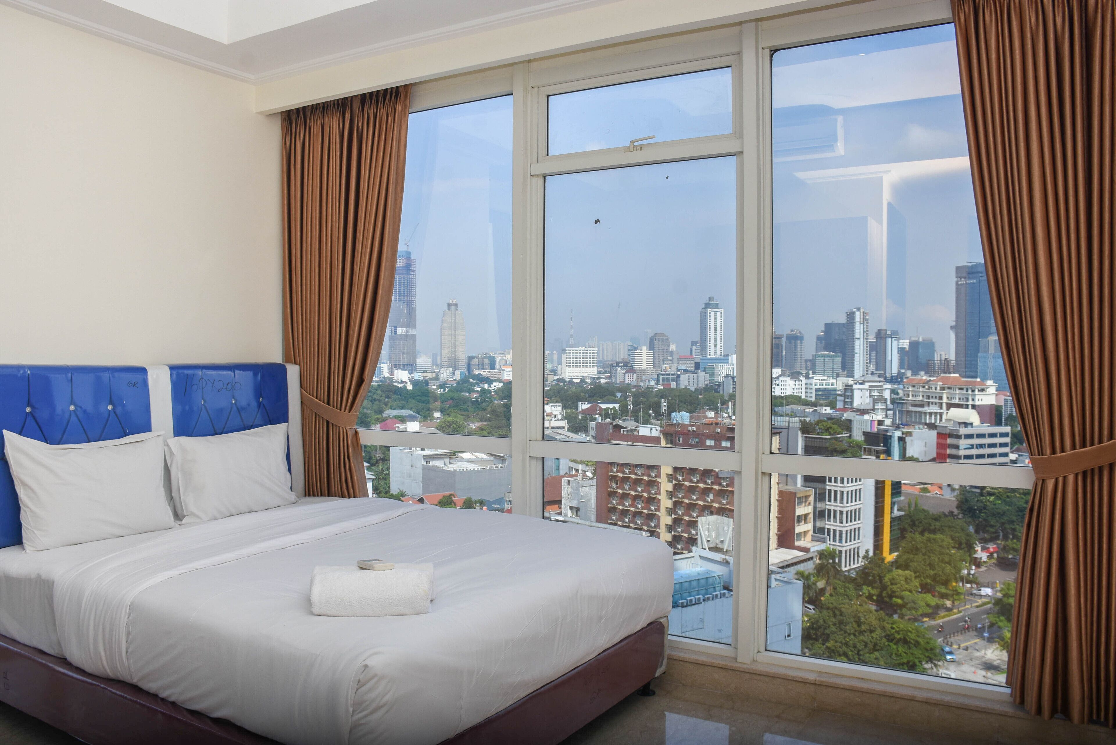 A hotel room with a large bed, white bedding, and a city view through large windows.
