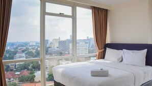 Hotellihuone, jossa on suuri sänky, ja jonka lattiasta kattoon ulottuvista ikkunoista avautuu näkymä kaupunkiin. Kaupungin siluetti on nähtävissä myös ulkona.