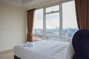 Ein Hotelzimmer mit einem großen Bett, Blick auf die Stadt und Vorhängen an den Fenstern.