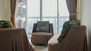 Een moderne woonkamer met twee banken en een fauteuil, grote ramen met gordijnen, en airconditioningsapparaten.