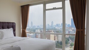 Een hotelkamer met een groot bed, uitzicht op een stadsbeeld door een groot raam en bruine gordijnen.