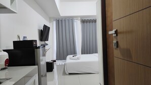 A hotel room with a bed, a desk with a computer, a television, and a water bottle on the desk. - Simply Homey Studio at Vida View Apartment (Makassar)