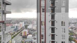 A high-rise building with multiple balconies, a view of a cityscape, and a cloudy sky. - Simply Homey Studio at Vida View Apartment (Makassar)